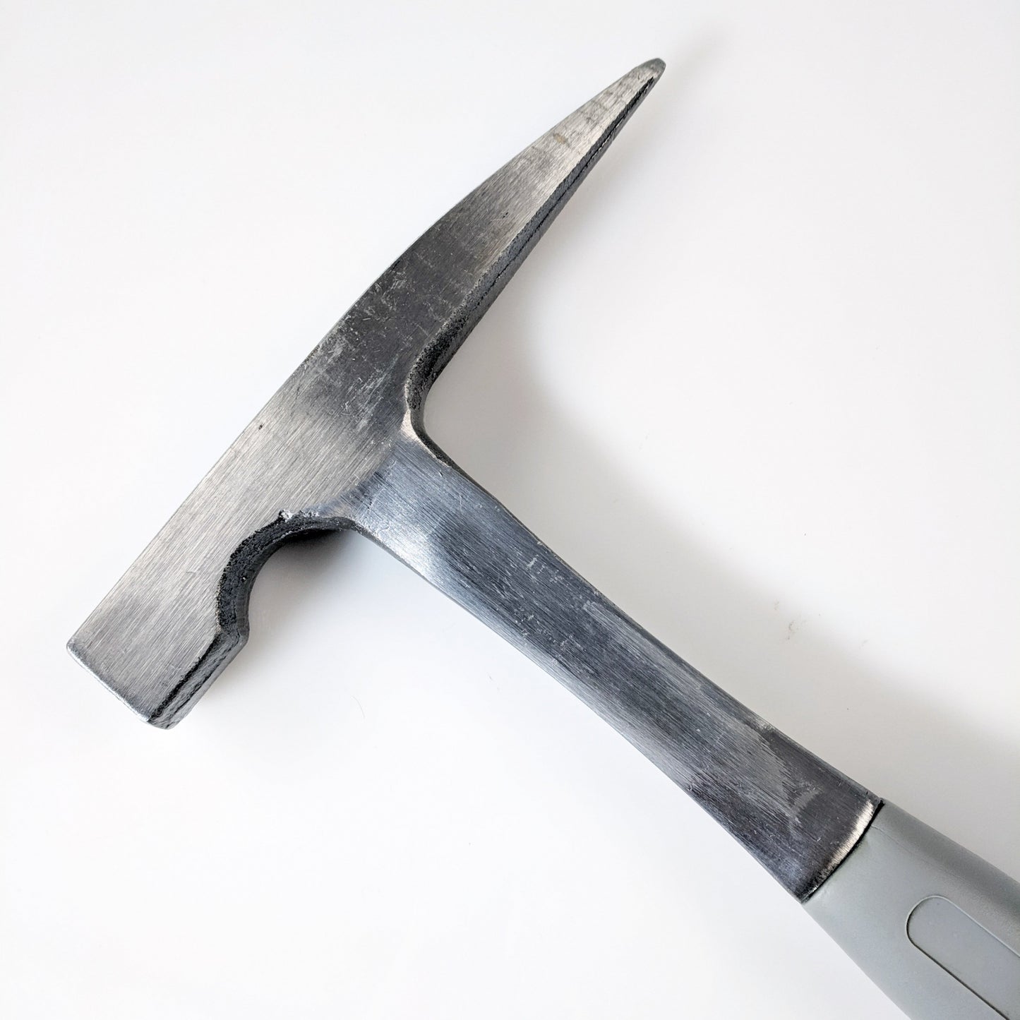 A silver-colored dual sided geology rock pick hammer with a pointed tip and rubberized grip handle, isolated on a white background.