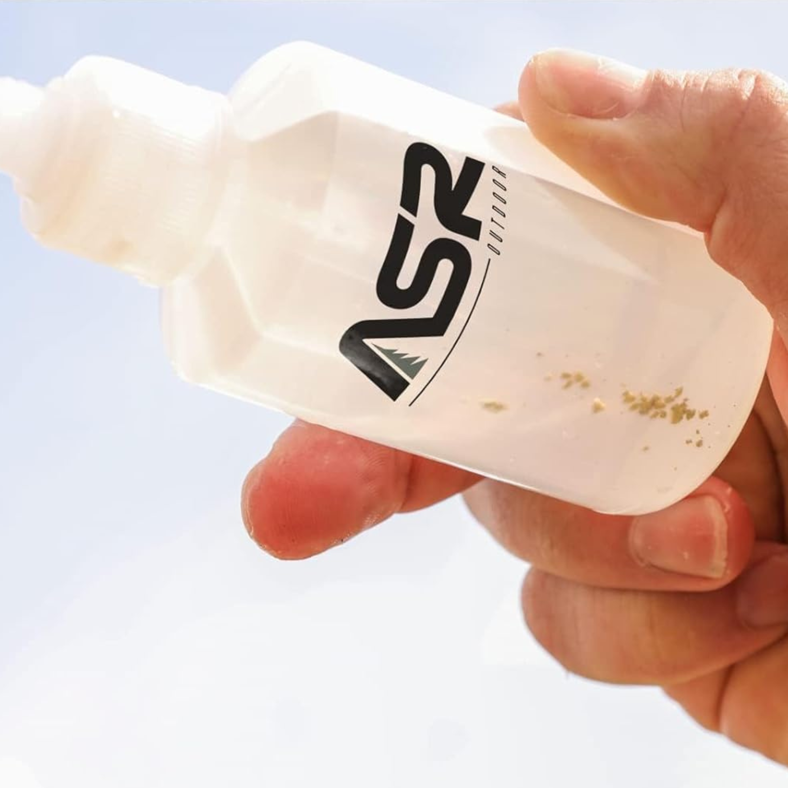 Hand holding a white ASR Outdoor snuffer bottle with a clear background