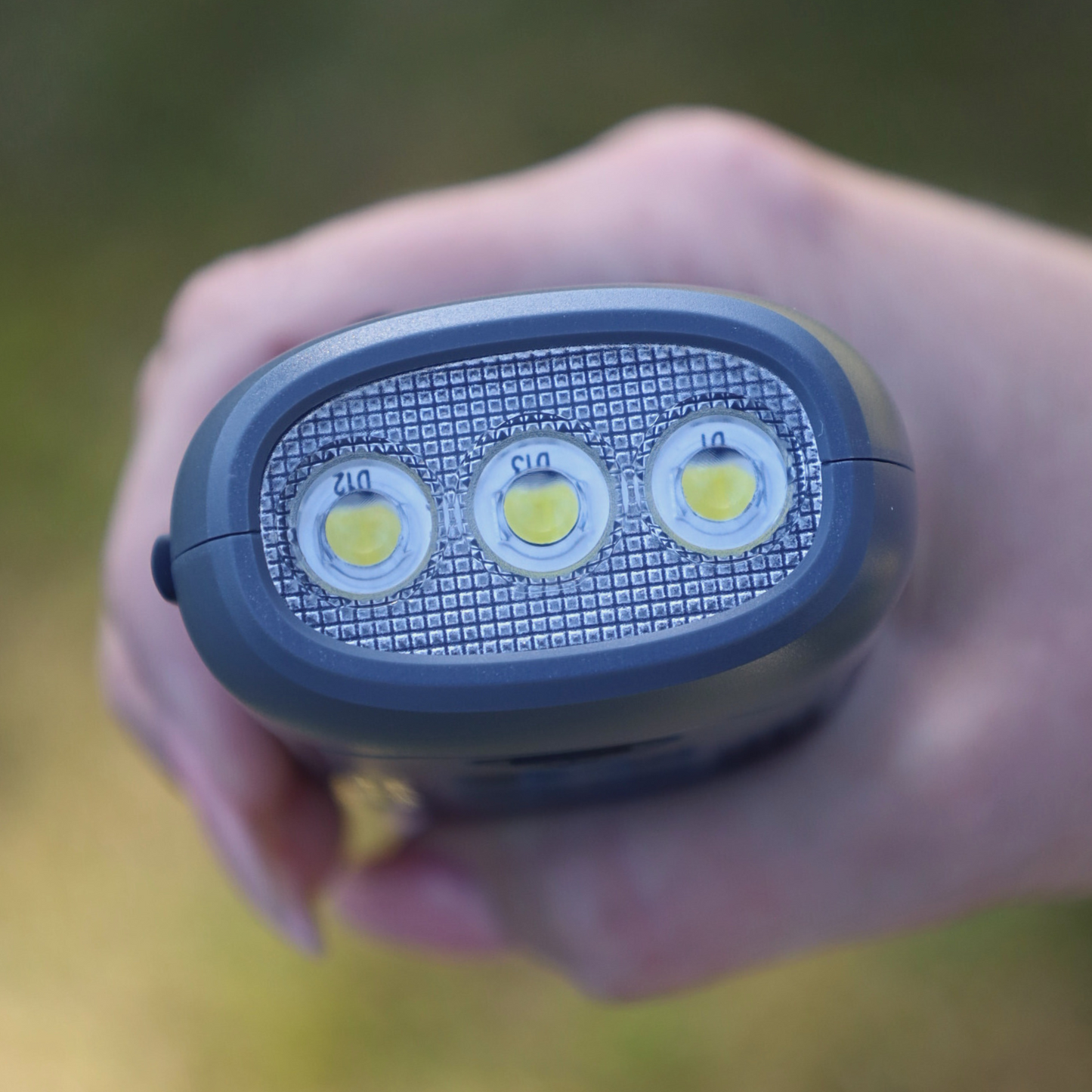 Hand holding a portable light source with three LED bulbs on a blurred natural background
