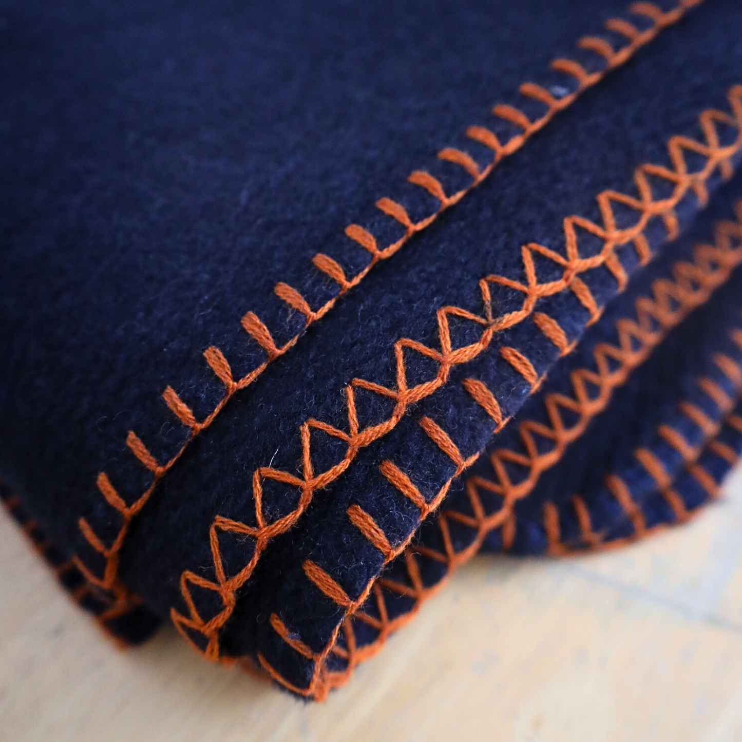 Close-up of blue fabric with orange stitching on a wooden surface