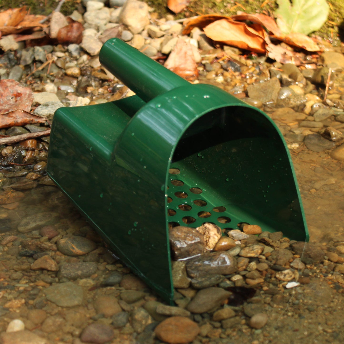 Green plastic scoop on a bed of small stones and leaves