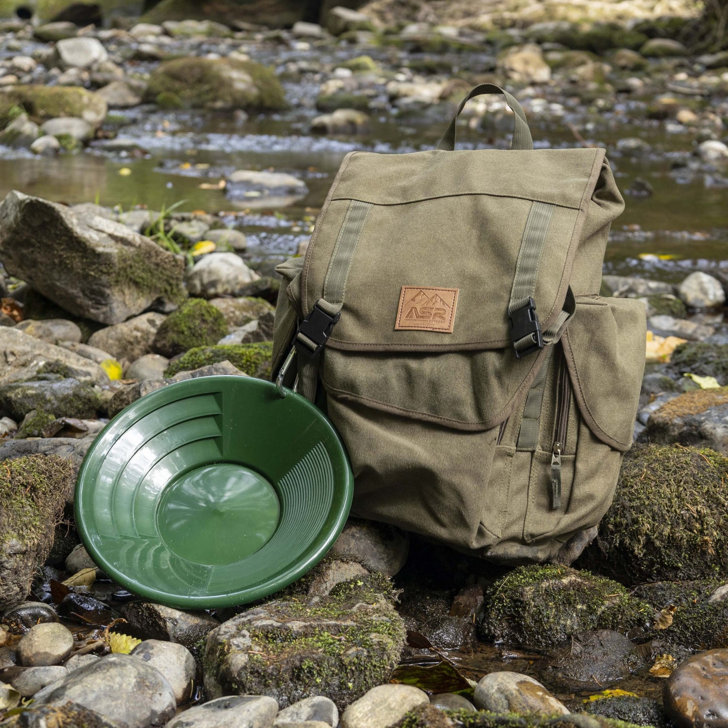 Backpack and green gold pan on a rocky stream bed