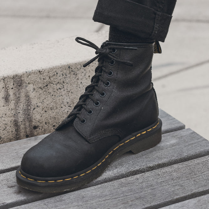 Black leather boot with yellow stitching on a wooden platform