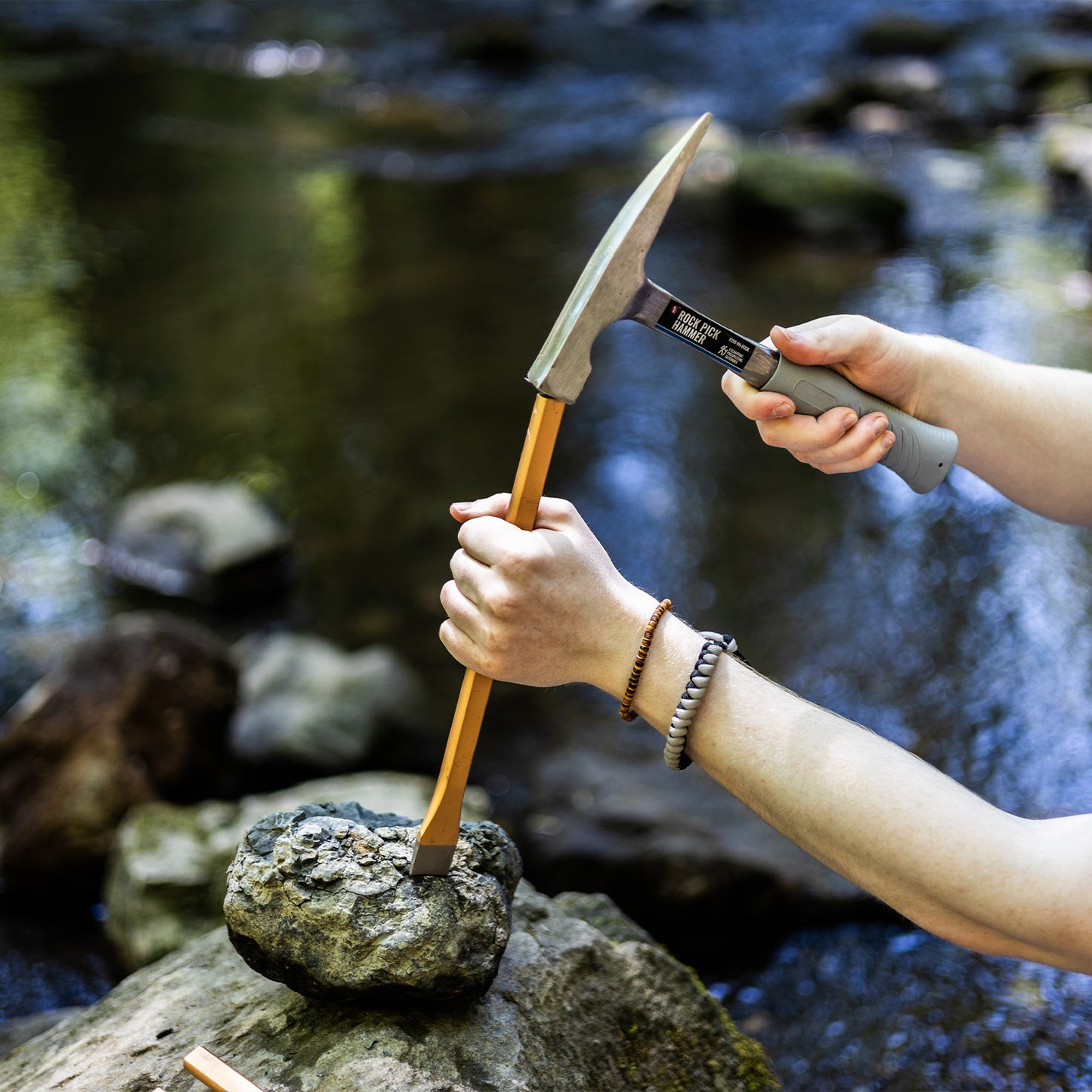 using a hammer to break open a geode next to a river
