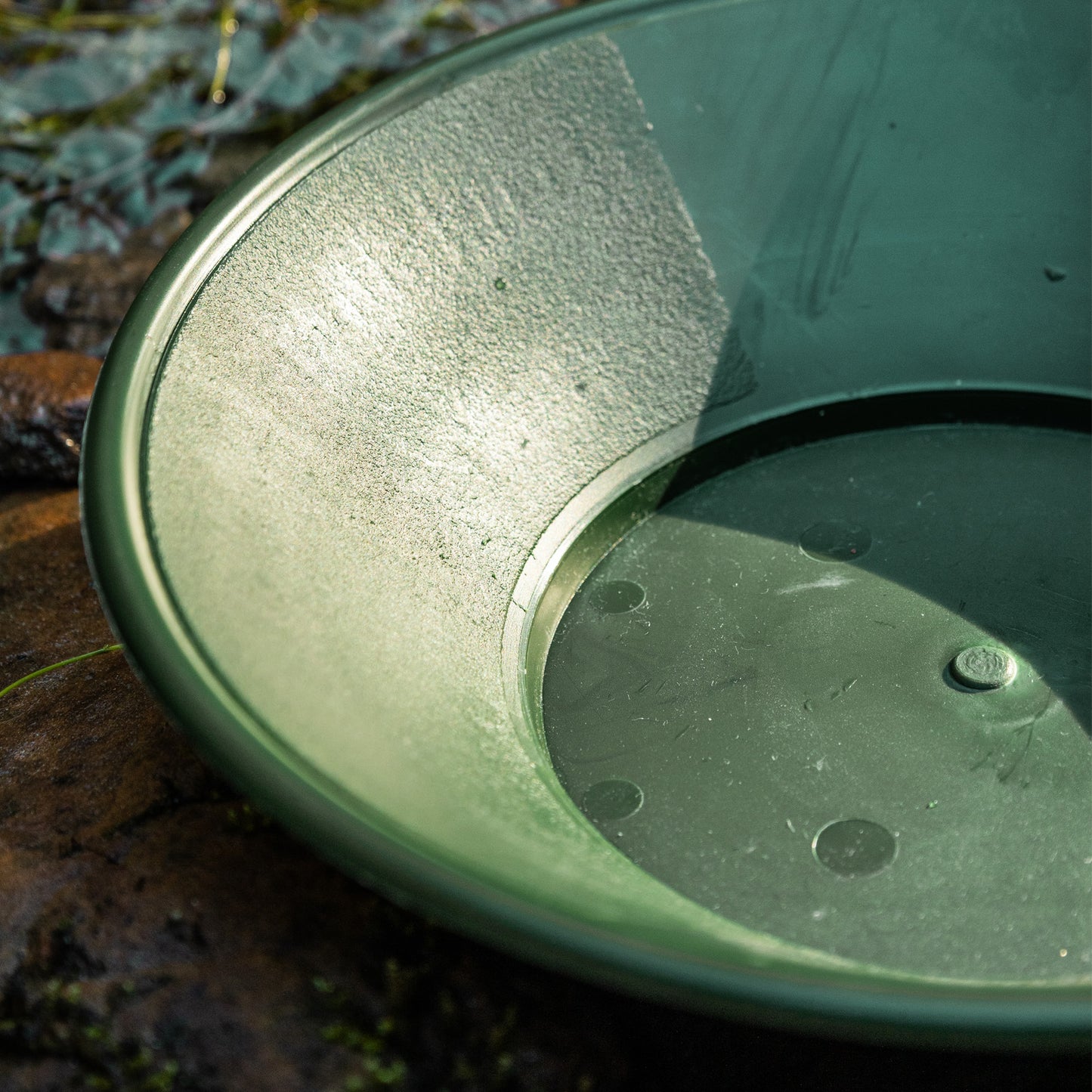 Close-up of a green single riffle gold pan with water droplets on a natural background