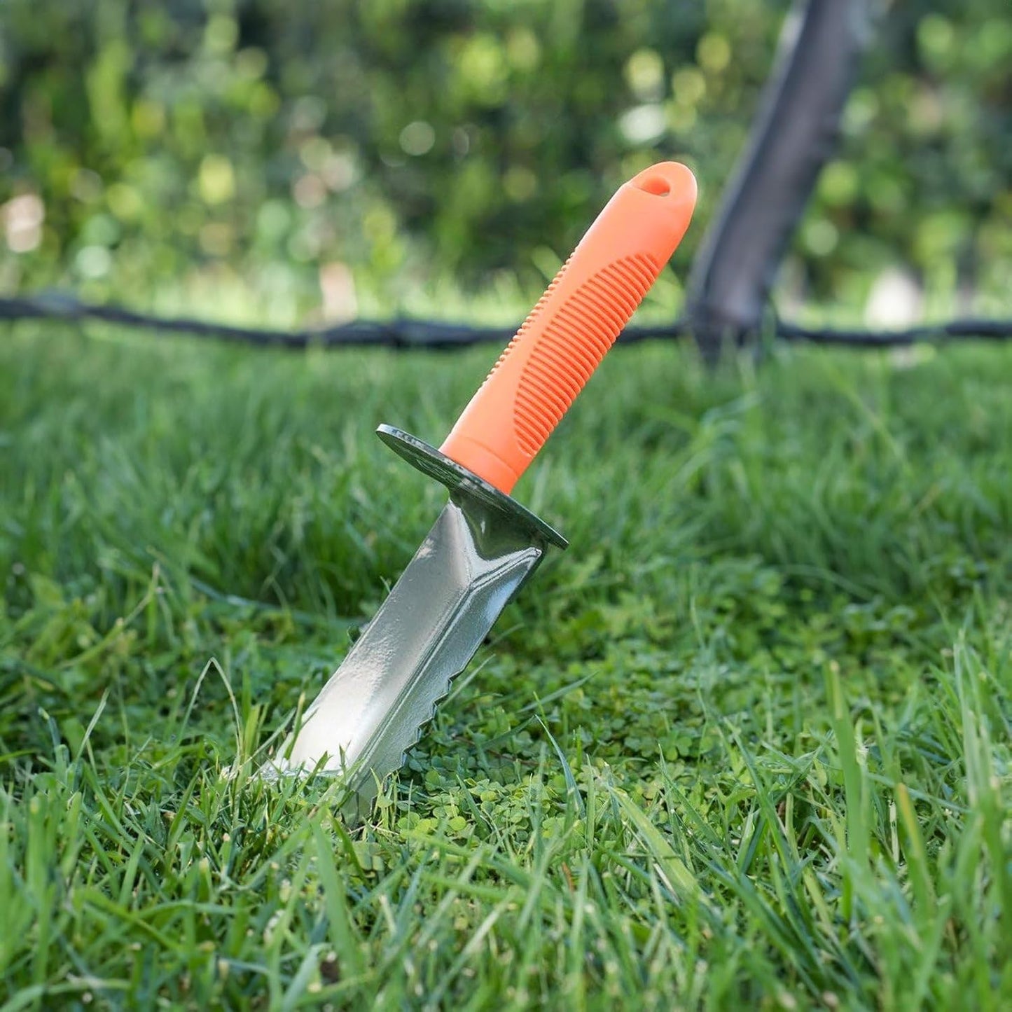 Orange-handled garden tool embedded in grass