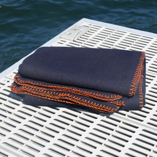 Folded navy blanket with orange stitching on a white dock by water