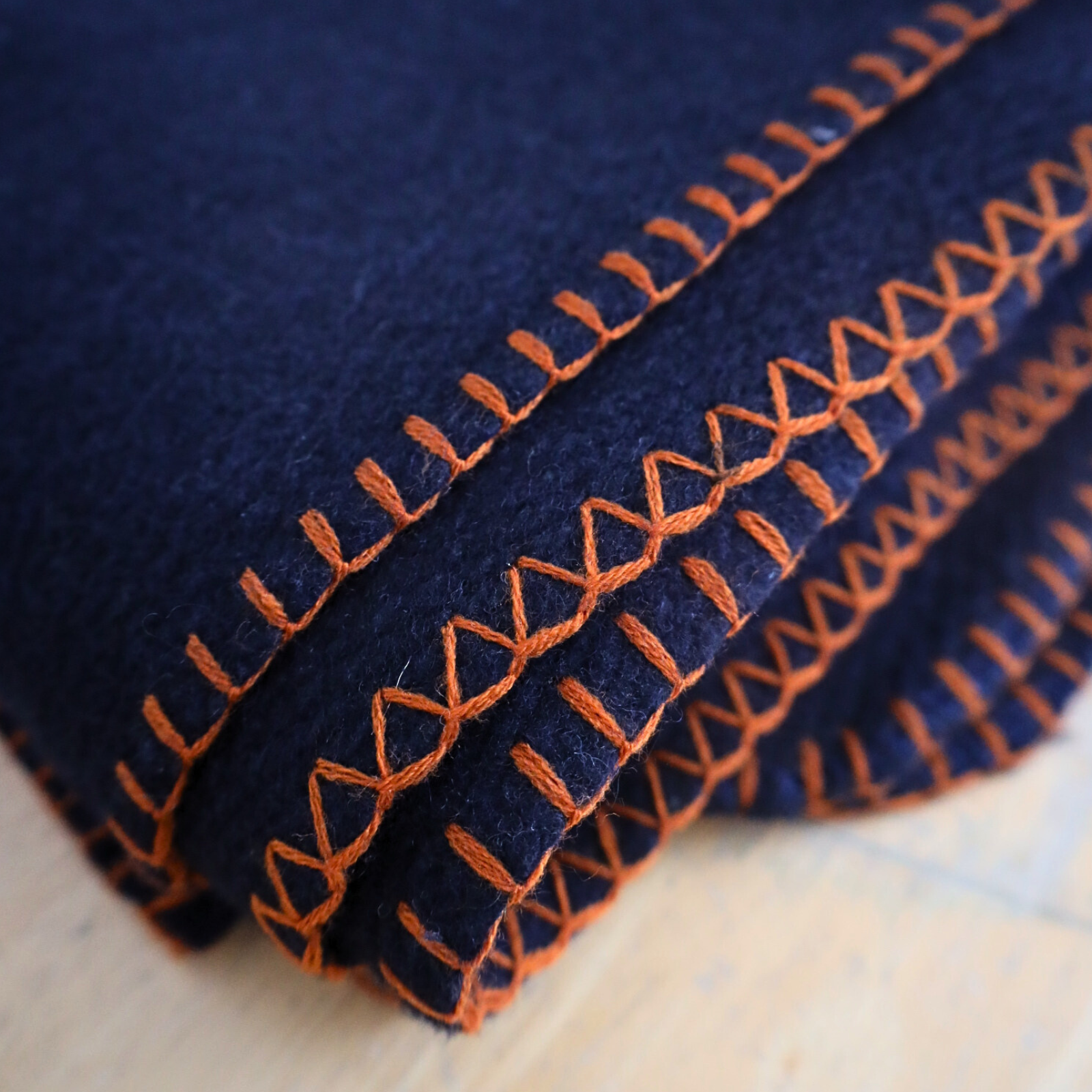 Close-up of blue fabric with orange stitching on a wooden surface