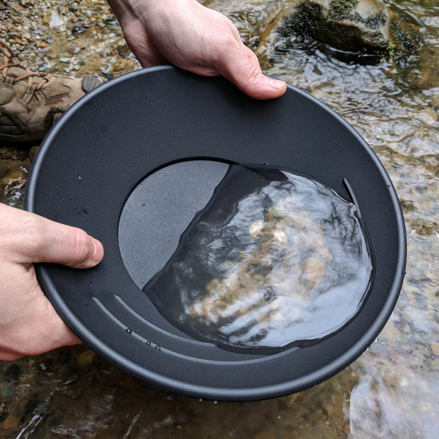 Lifestyle shot of the black traditional single riffle gold pan being used by a river.