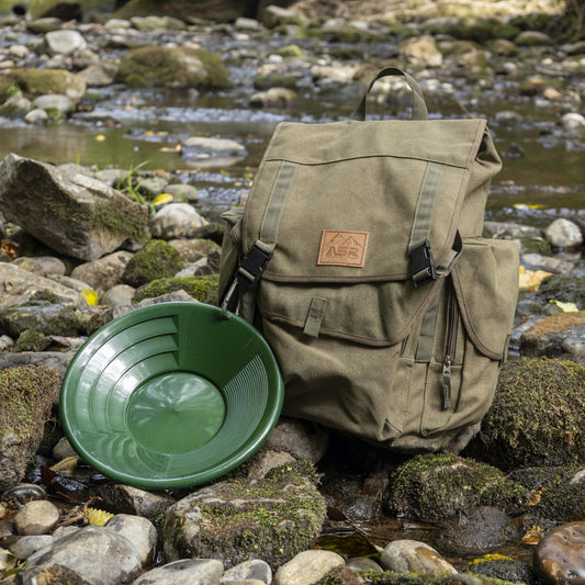 gold panning backpack with green gold pan in a forest river