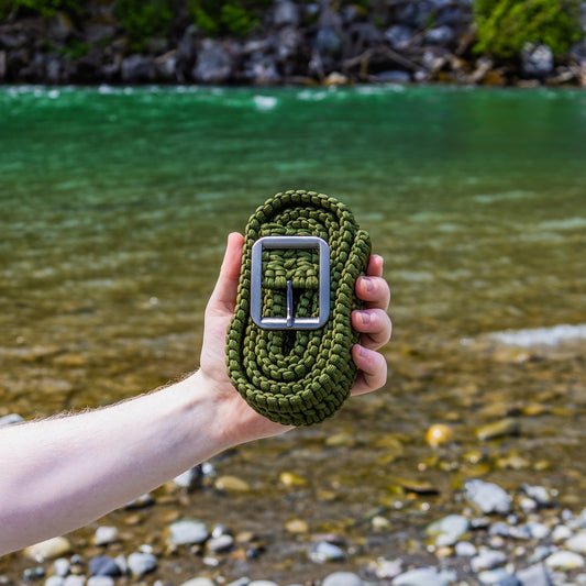 Hand holding a green belt with a silver buckle against a natural blue river background