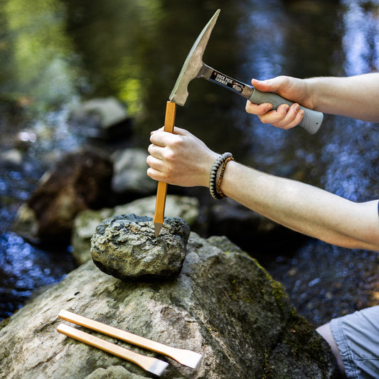 Person using a hammer and chisel on a rock by a stream