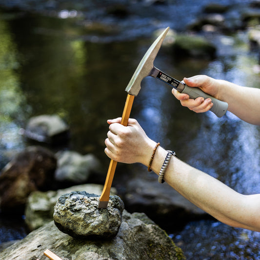 using a hammer to break open a geode next to a river